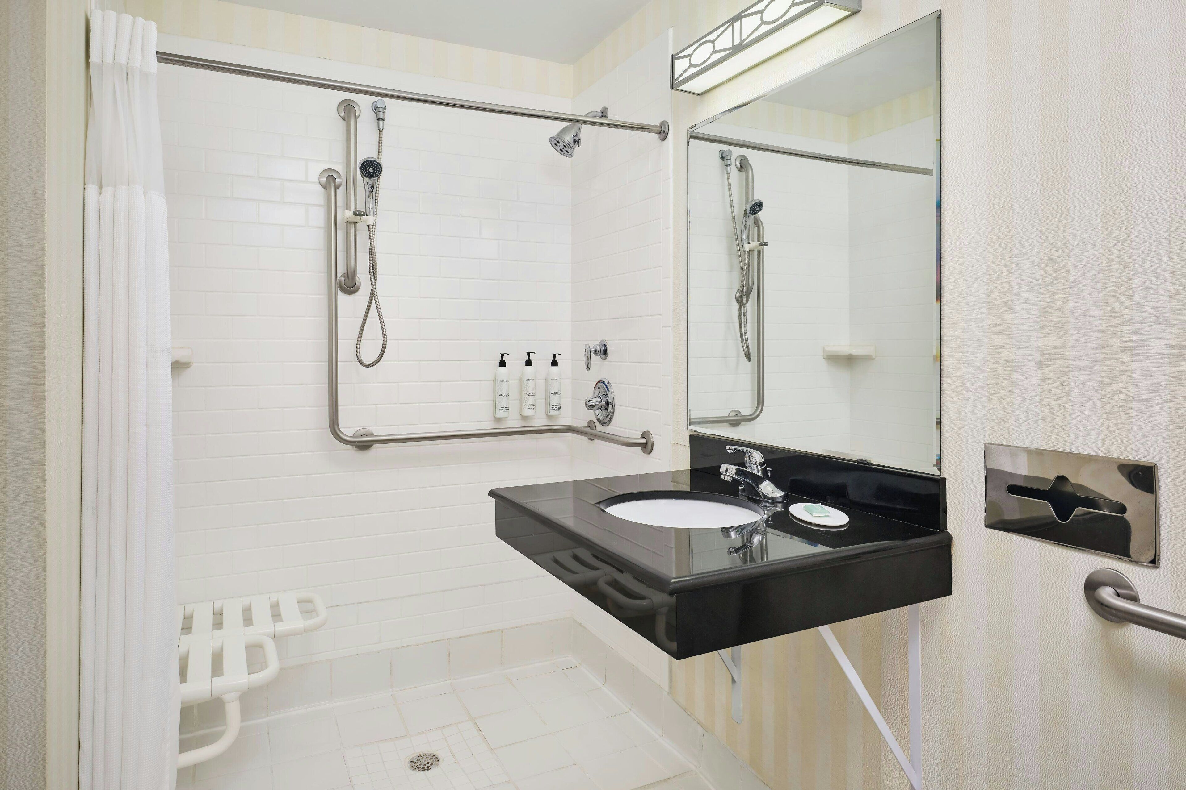 A bathroom with a white tiled shower, a black sink, and a mirror.
