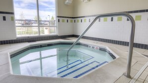 A swimming pool with a metal ladder, tiled walls, and a view of a parking lot through a large window. - Fairfield Inn & Suites by Marriott Laramie (Laramie)