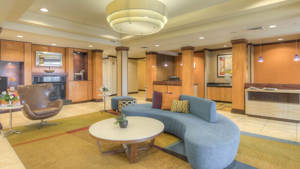 A modern lobby with a curved sofa, a round coffee table, and a seating area with a brown leather chair. - Fairfield Inn & Suites by Marriott Laramie (Laramie)