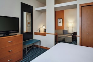 A hotel room with a bed, a desk with a chair, a television, a lamp, a sofa, and a door. - Fairfield Inn & Suites by Marriott Laramie (Laramie)