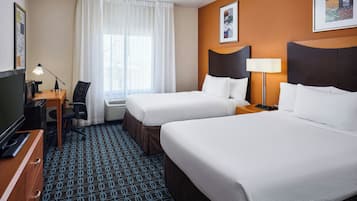 A hotel room with two beds, a desk with a lamp, a television, and a chair.