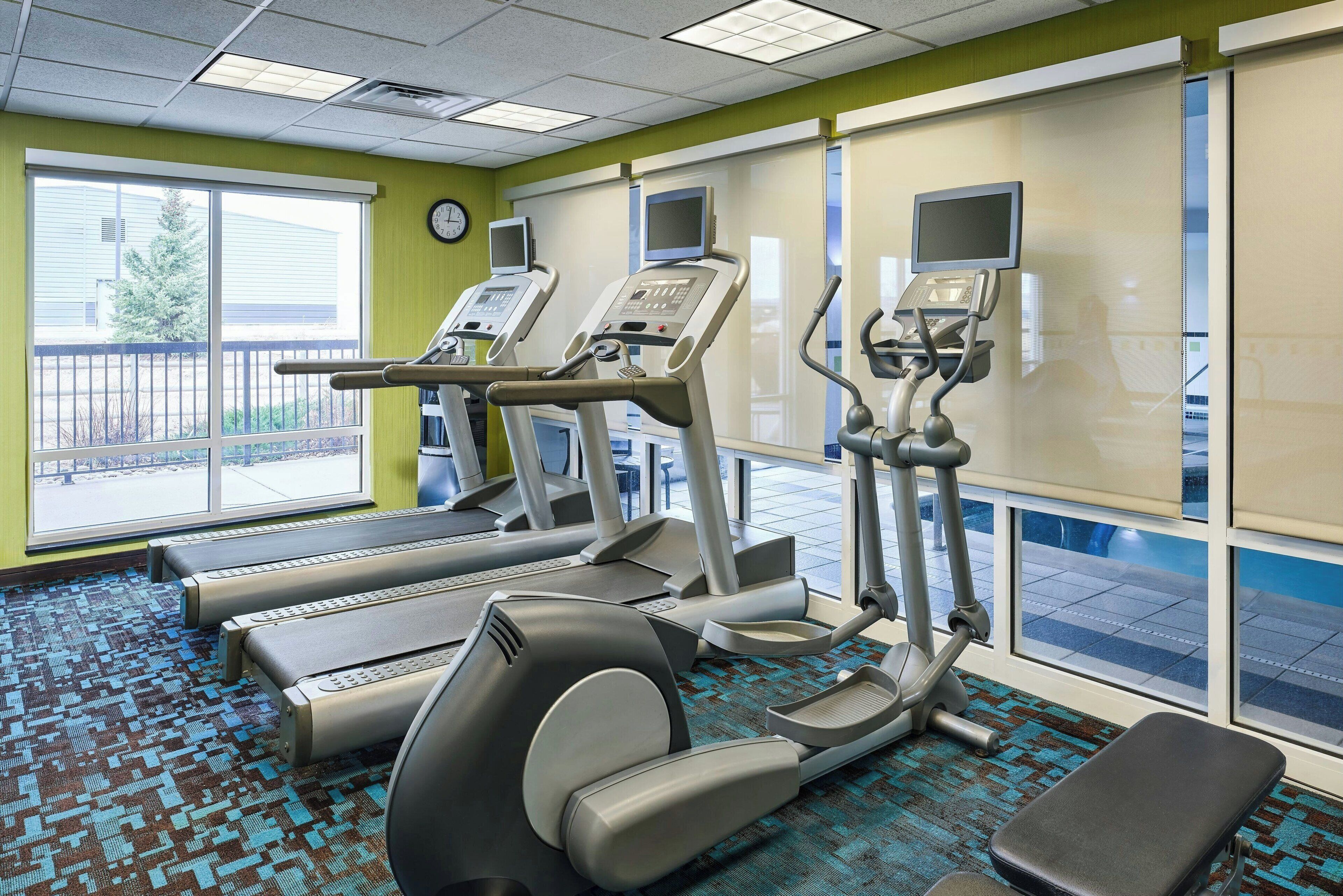 A fitness center with treadmills, elliptical machines, and a bench.