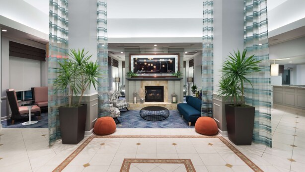 A spacious lobby with a fireplace, seating area, and large potted plants. - Hilton Garden Inn Frisco (Frisco)