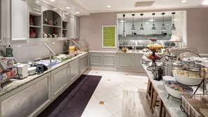 A modern kitchen with a marble countertop, a buffet area with various food items, and a decorative shelf with pottery. - Hilton Garden Inn Frisco (Frisco)
