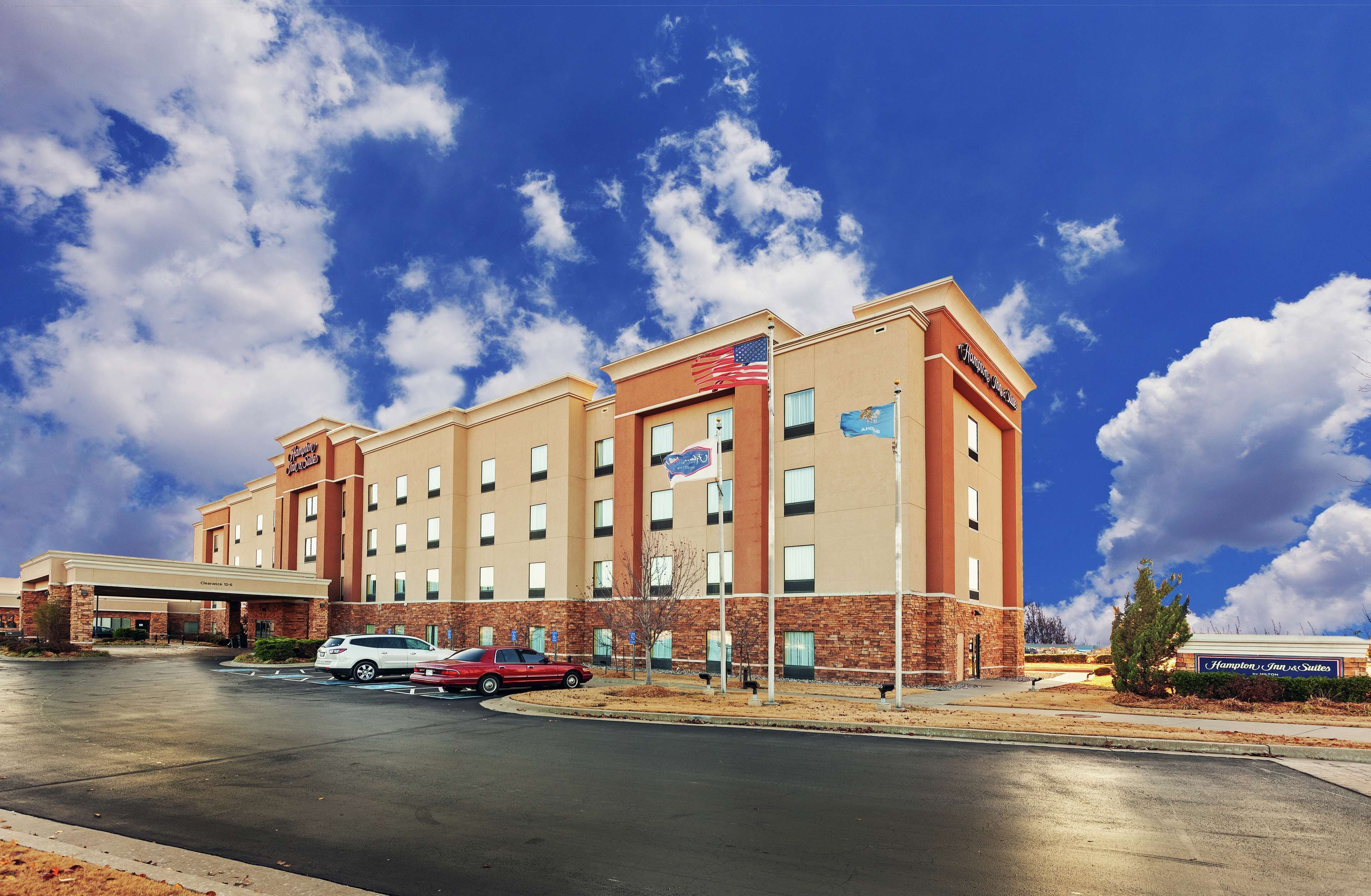 A multi-story hotel with a brick facade, multiple windows, and a parking lot with several cars.