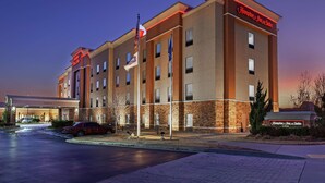 A Hampton Inn Suites building with a brick facade, multiple windows, and an American flag. - Hampton Inn & Suites Tulsa North/Owasso (Owasso)