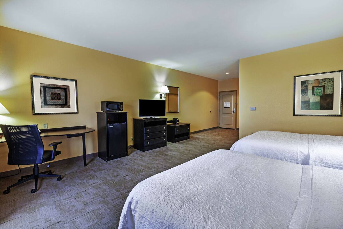 A hotel room with two beds, a desk, a chair, a television, and a lamp.