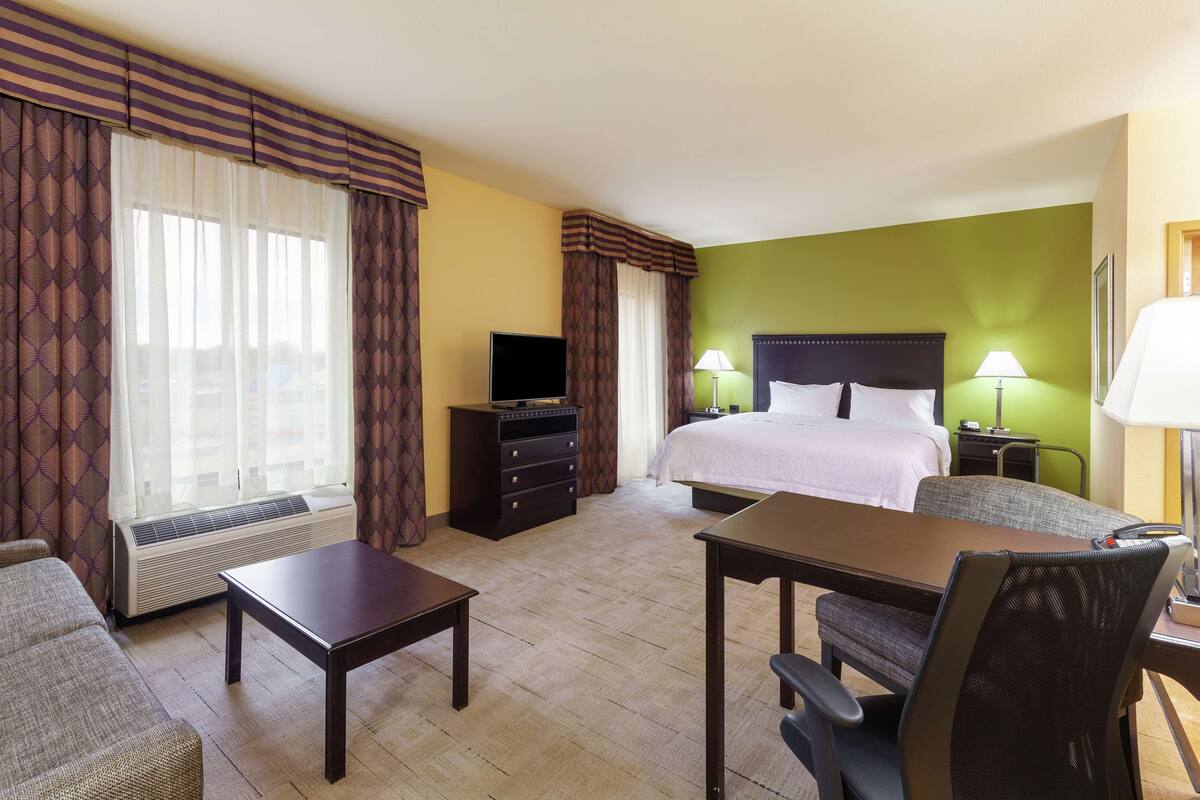 A hotel room with a bed, a desk, a chair, a television, and a window with curtains.