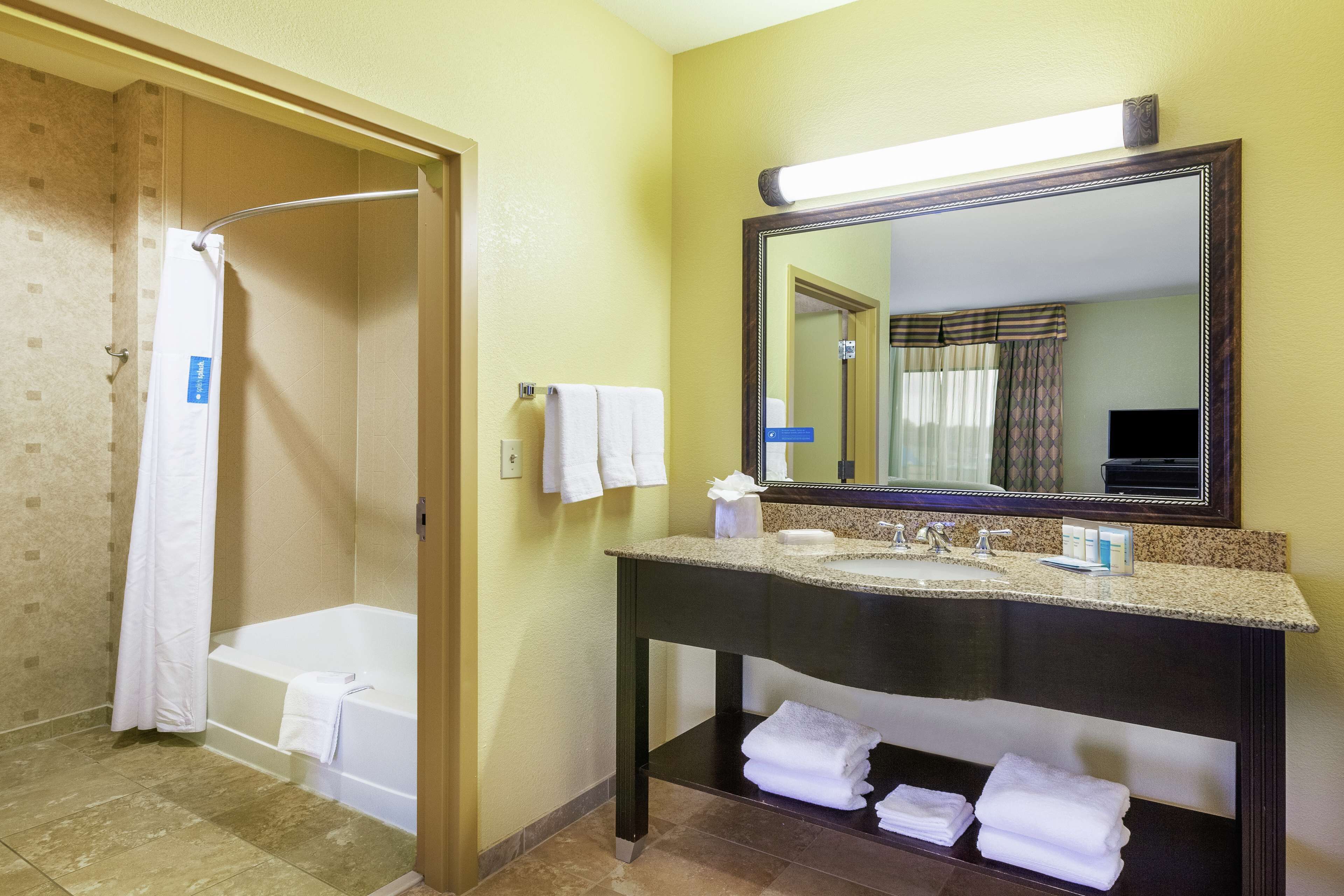 A bathroom with a bathtub, a sink with a mirror, and towels on the counter.