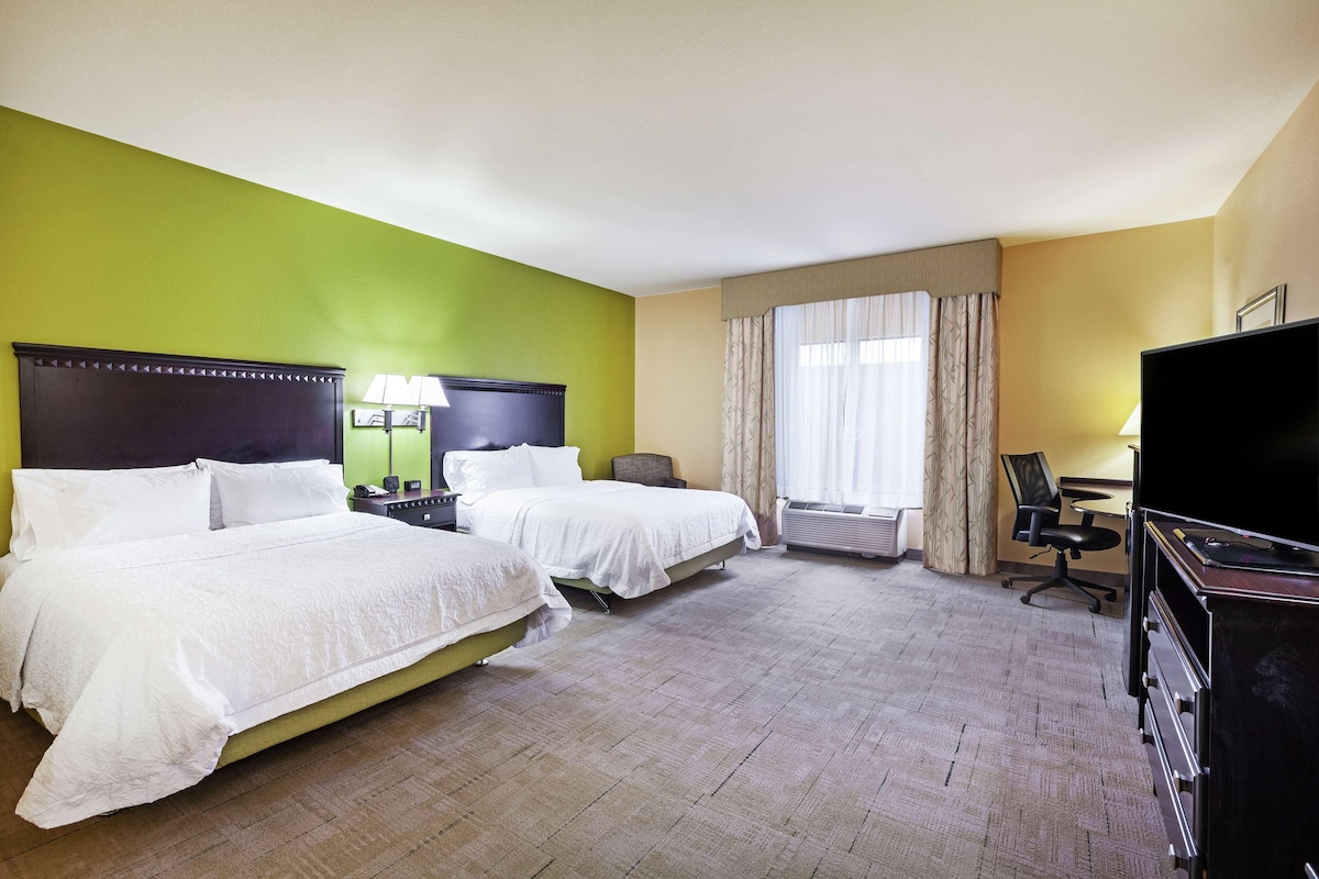 A hotel room with two beds, a desk, a chair, and a television.