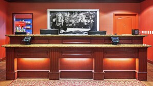 A reception desk with a digital phone, a large screen displaying a woman with bubbles, and a red wall. - Hampton Inn & Suites Tulsa North/Owasso (Owasso)
