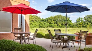 Une terrasse extérieure avec deux tables et des chaises, deux parasols et un bâtiment en briques en arrière-plan.