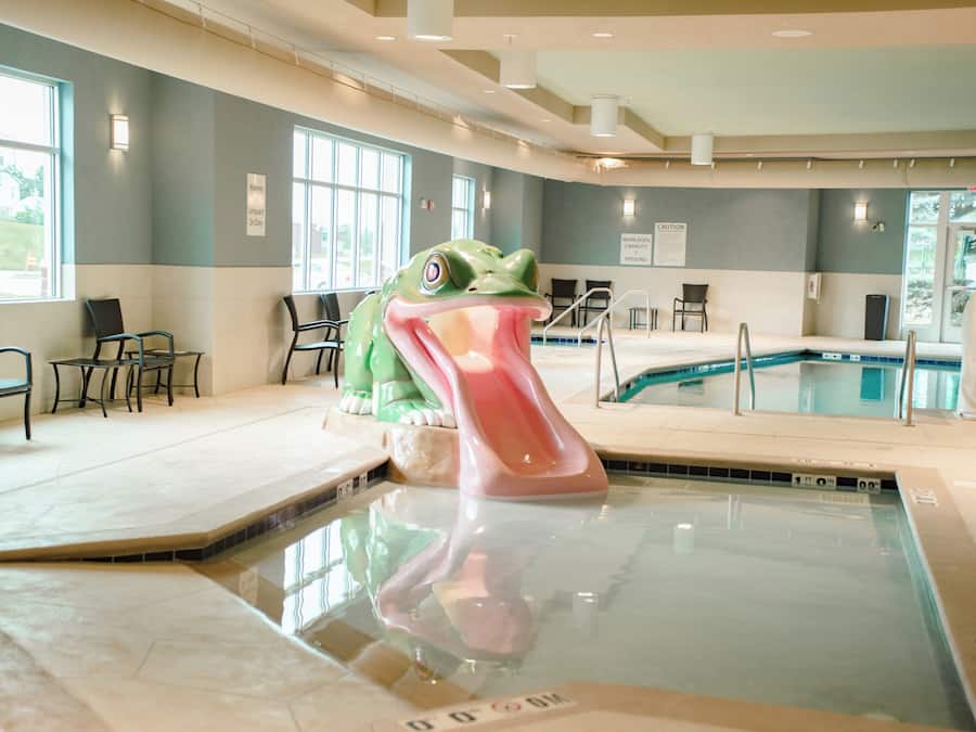 An indoor swimming pool with a lifeguard chair, a frog sculpture, and a whirlpool capacity sign.