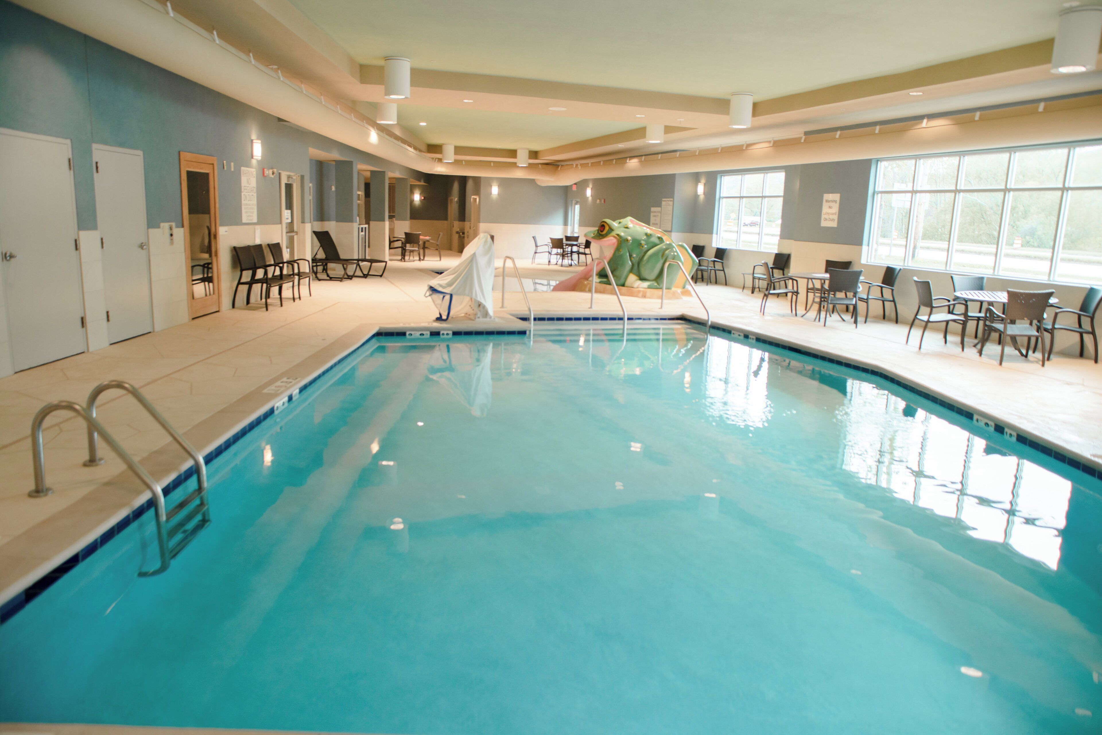 An indoor swimming pool with a slide, lounge chairs, and a frog statue.