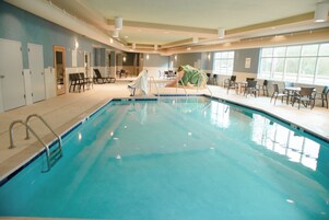 An indoor swimming pool with a slide, lounge chairs, and a frog statue.