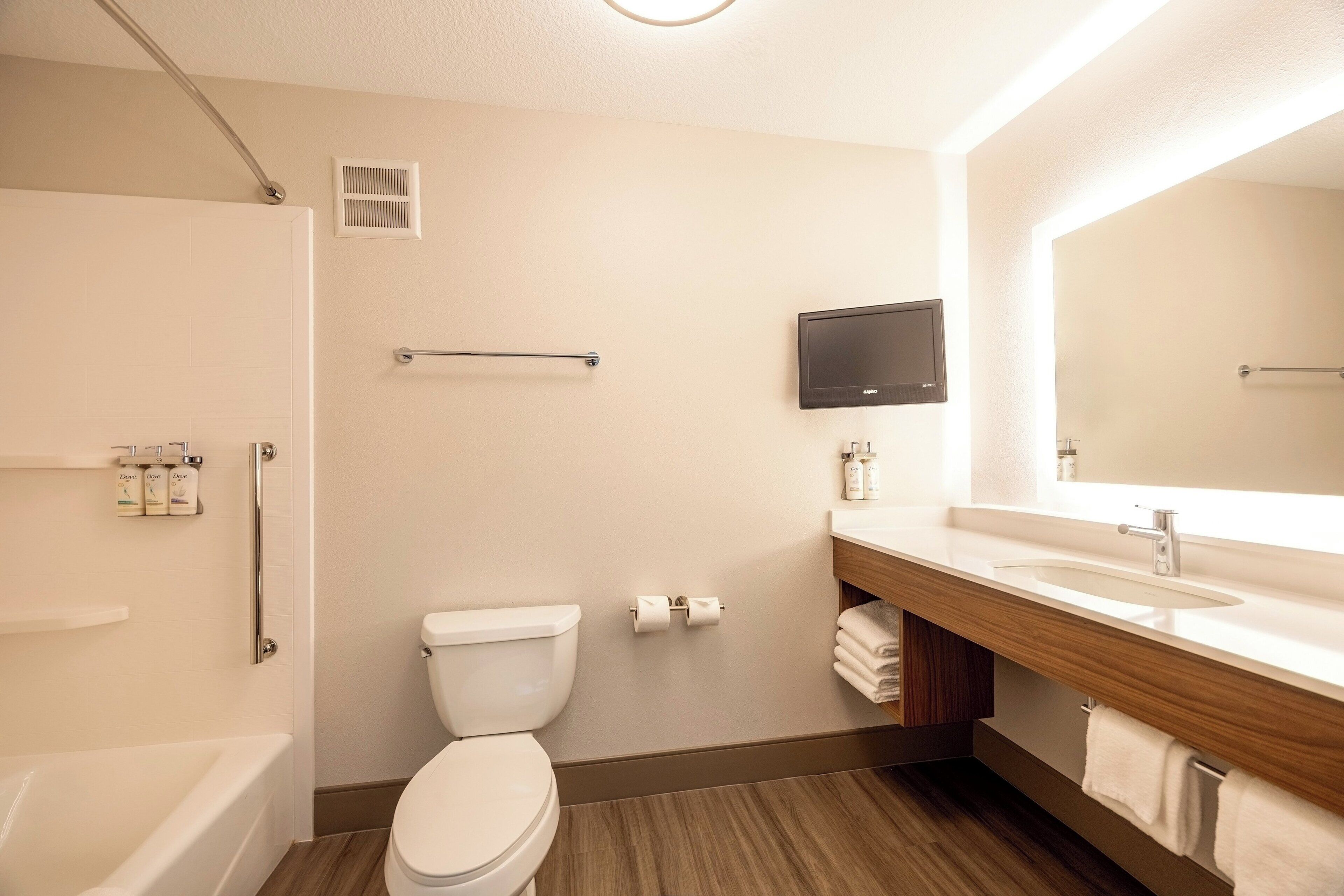 A modern bathroom with a toilet, sink, shower, and a mounted TV.
