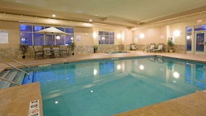 A hotel indoor pool with clear water, lounge chairs, and a seating area with an umbrella. - Holiday Inn Express & Suites Winona by IHG (Winona)