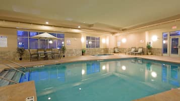 A hotel indoor pool with clear water, lounge chairs, and a seating area with an umbrella.