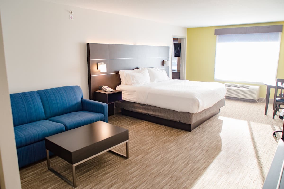 A hotel room with a bed, a blue sofa, a small table, a nightstand, and a wall-mounted lamp.