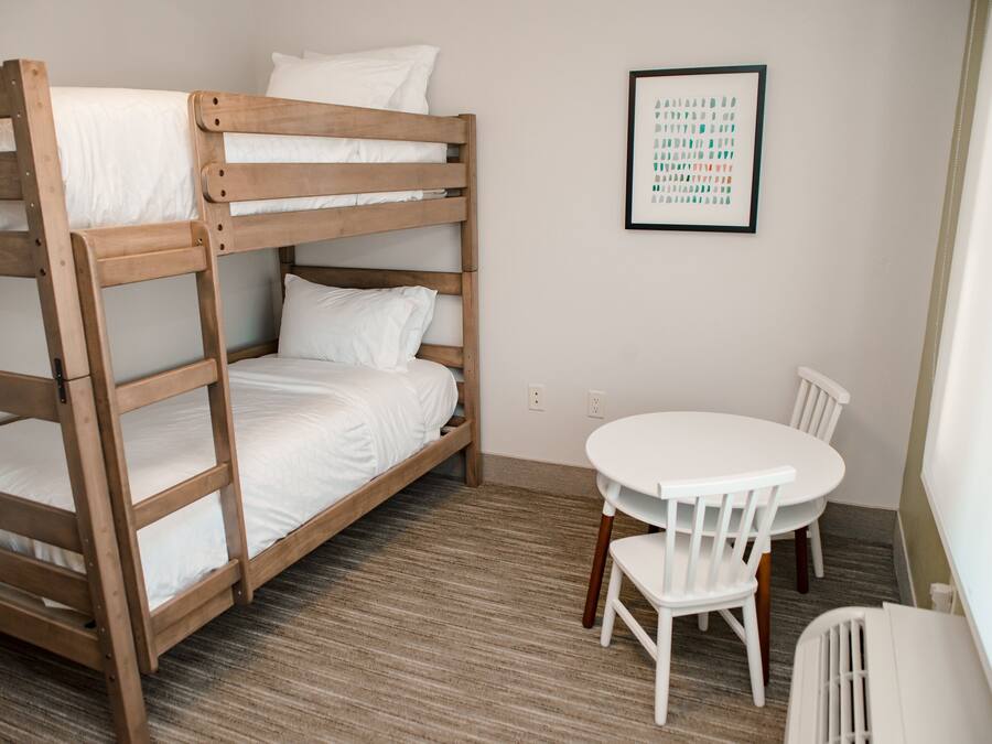 A bunk bed with white bedding, a small round table with chairs, and a framed picture on the wall.