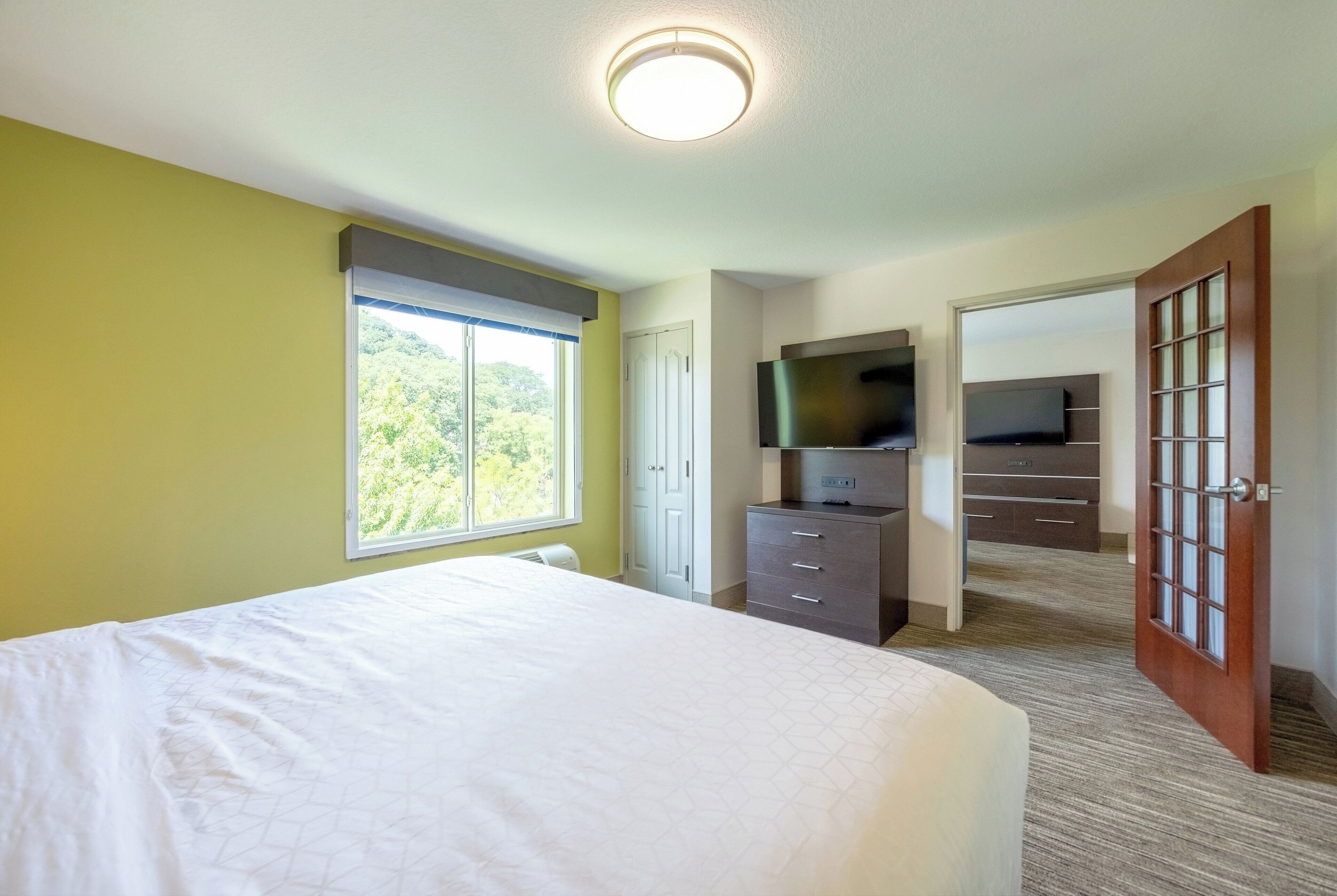 A hotel room with a large bed, a TV, a wardrobe, and a door leading to another room.