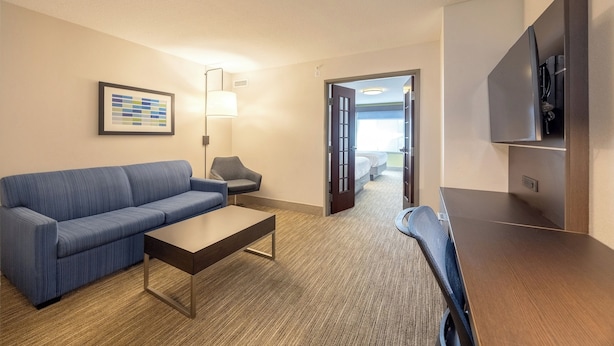A hotel room with a blue sofa, a wooden coffee table, a lamp, a TV, and a door leading to a balcony. - Holiday Inn Express & Suites Winona by IHG (Winona)