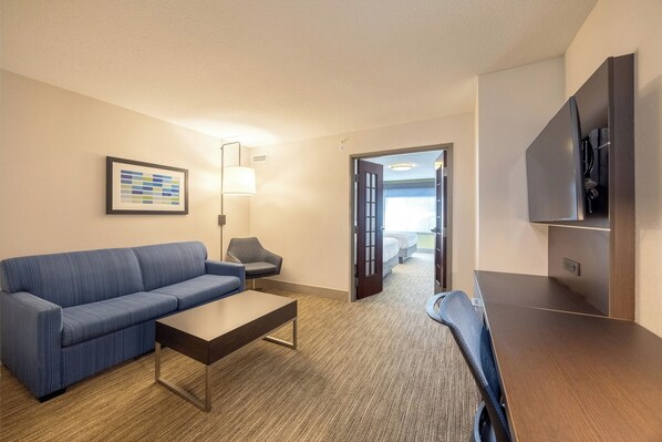 A hotel room with a blue sofa, a wooden coffee table, a lamp, a TV, and a door leading to a balcony. - Holiday Inn Express & Suites Winona by IHG (Winona)