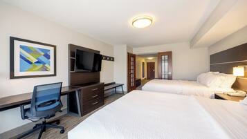 Ein Hotelzimmer mit Schreibtisch, zwei Betten, einem Fernseher und einem gerahmten Kunstwerk an der Wand.