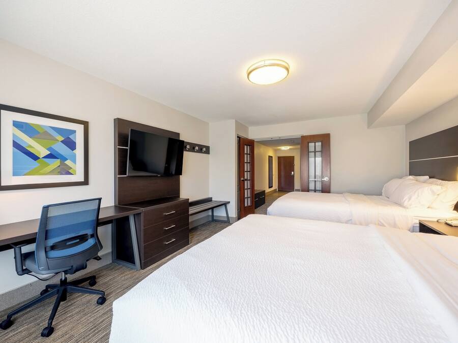 Ein Hotelzimmer mit Schreibtisch, zwei Betten, einem Fernseher und einem gerahmten Kunstwerk an der Wand.