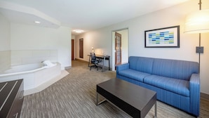 Une chambre d’hôtel moderne avec une grande baignoire, un canapé bleu, un bureau avec une chaise et une œuvre d’art encadrée au mur.