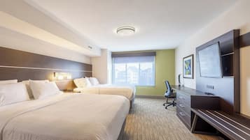 A hotel room with two beds, a desk, a chair, a flat-screen TV, and a window with a view of buildings.