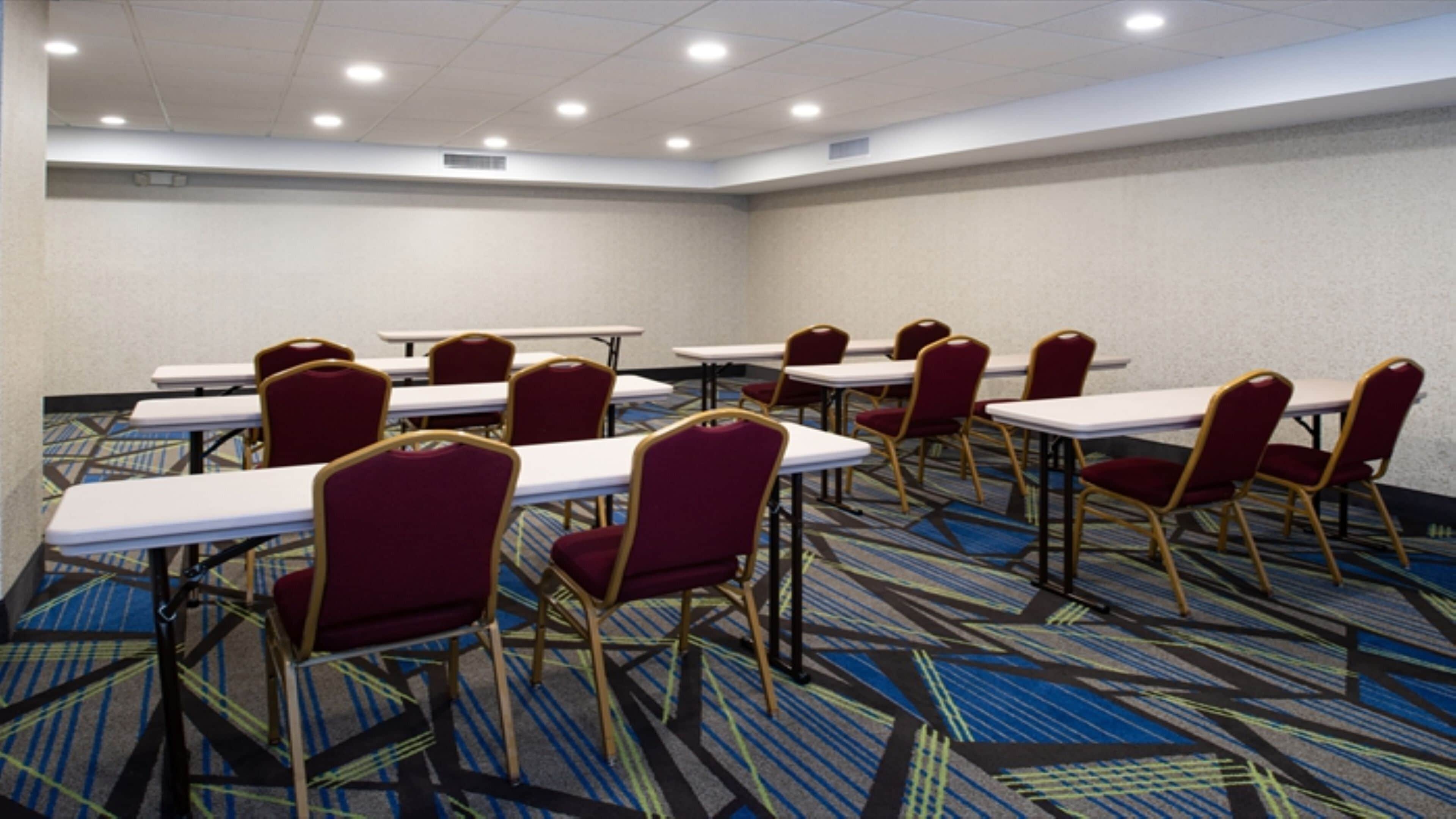 Un salón de conferencias con mesas y sillas, piso alfombrado e iluminación en el techo.