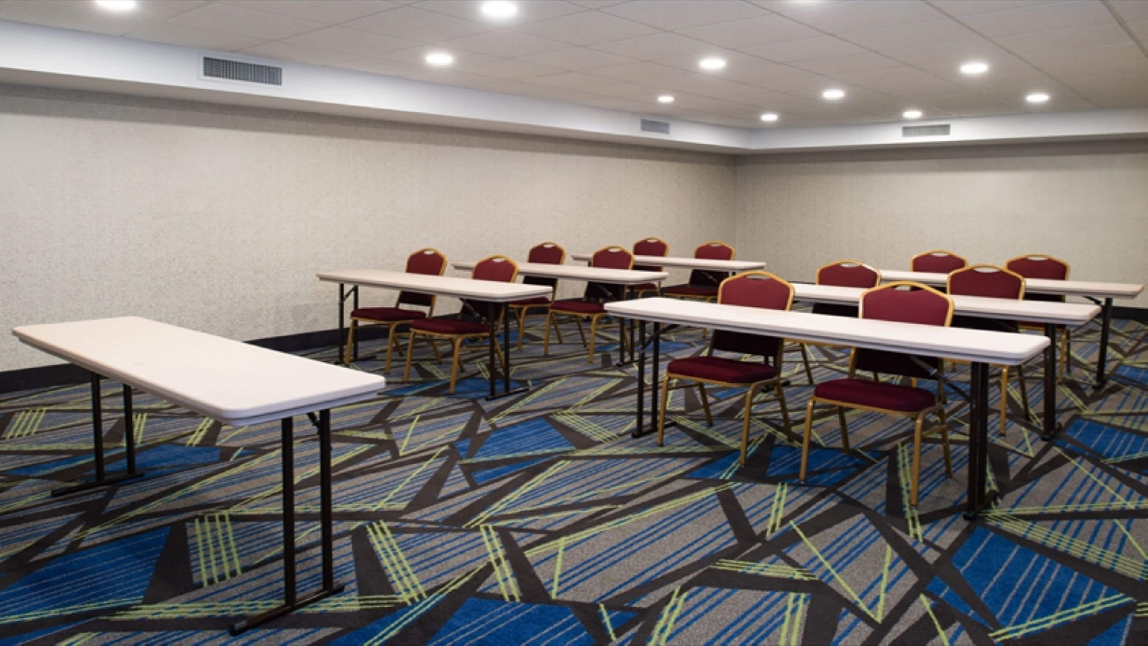 Une salle de conférence dotée de plusieurs tables et chaises, d’un sol recouvert de moquette et d’un éclairage au plafond.
