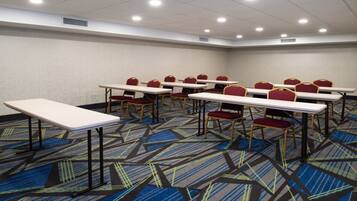 Une salle de conférence dotée de plusieurs tables et chaises, d’un sol recouvert de moquette et d’un éclairage au plafond.
