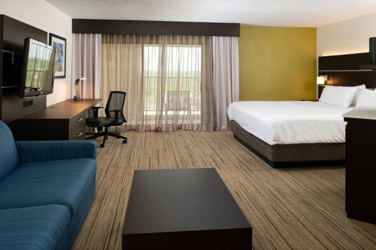 A hotel room with a bed, a desk, a chair, a TV, and a sofa.