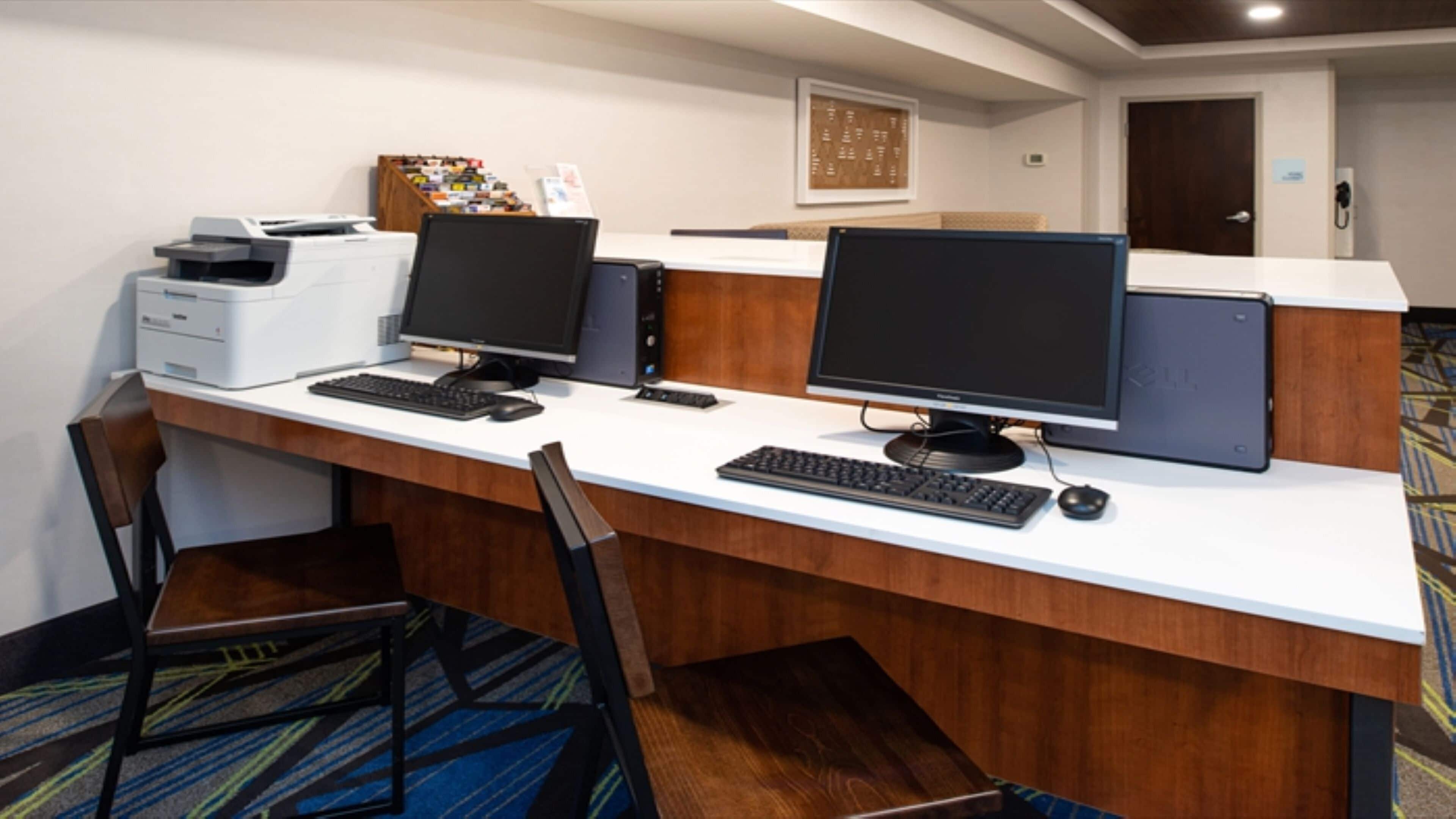 Espaço de trabalho em hotel com duas estações de computador, uma impressora e uma cadeira.