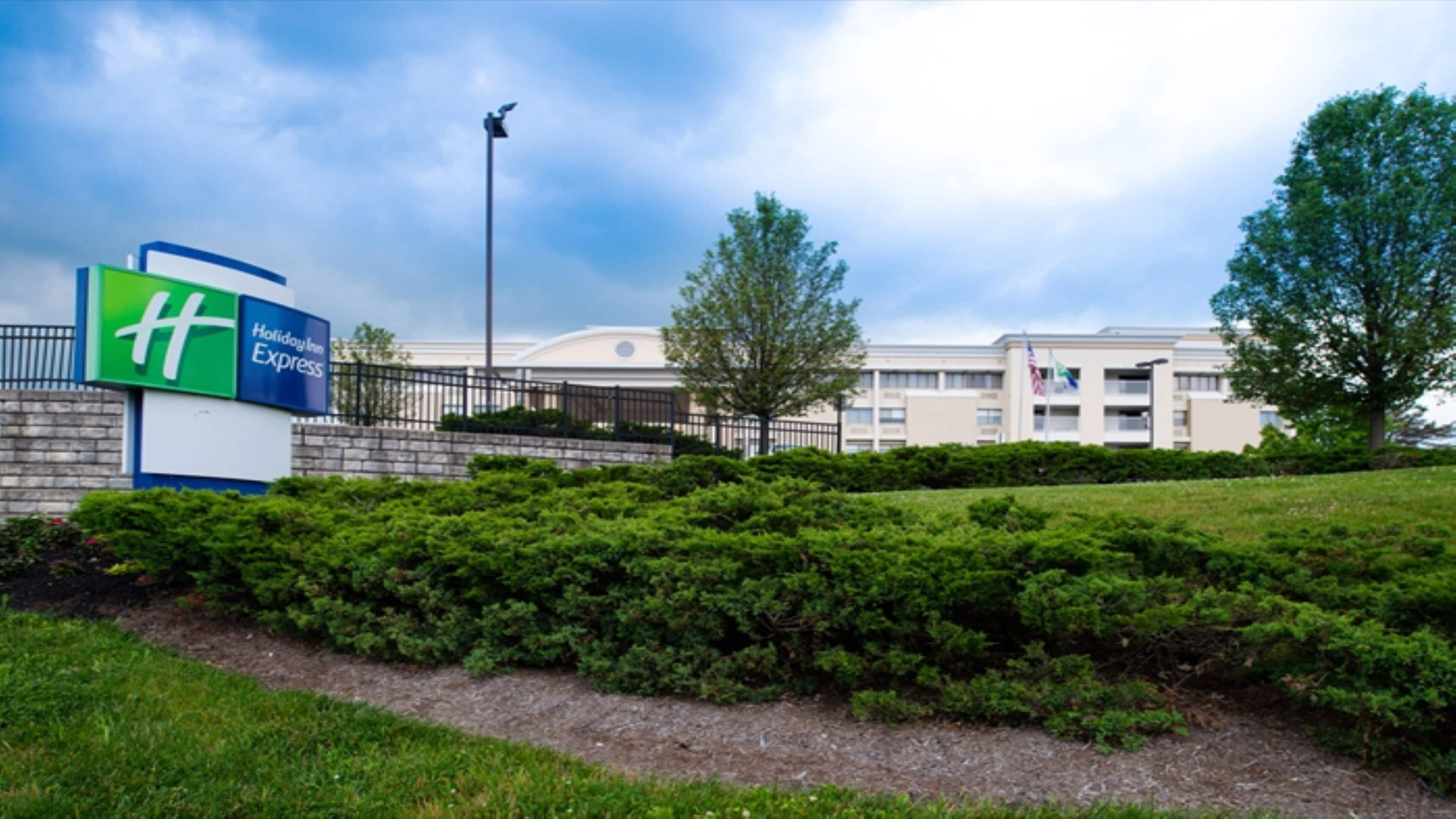 Une enseigne Holiday Inn Express, avec un espace paysager aménagé devant, un lampadaire et un bâtiment en arrière-plan.