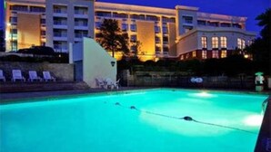 A hotel with a swimming pool, lounge chairs, and a large building in the background.