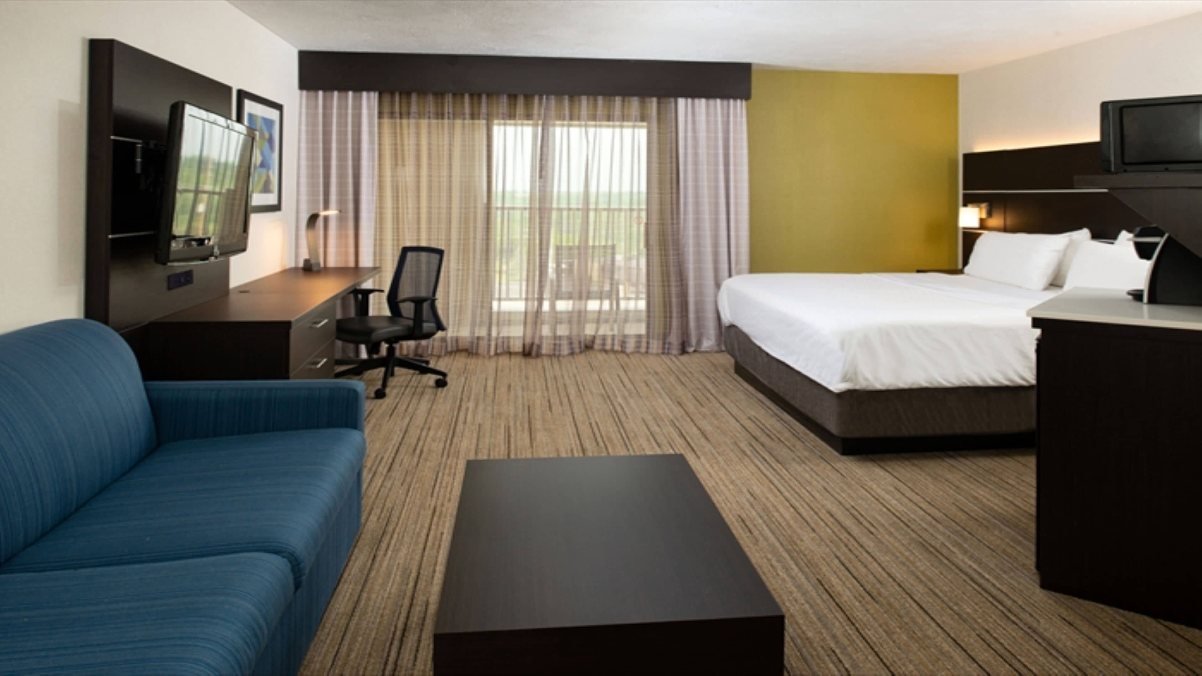 A hotel room with a bed, a desk, a chair, a sofa, and a television.