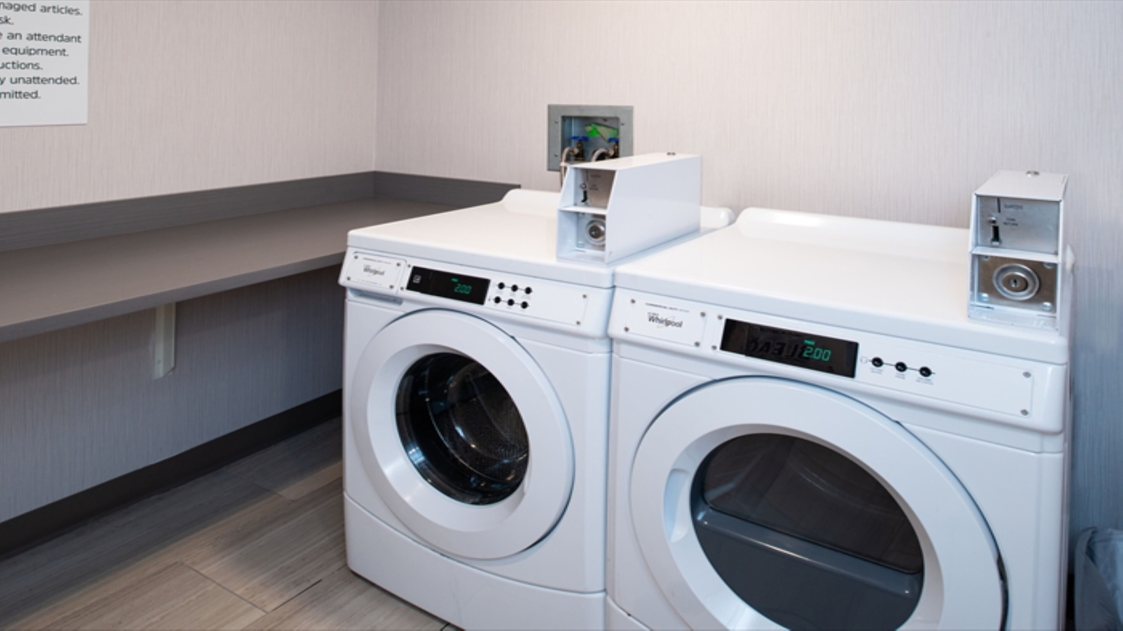 A laundry area with two front-loading washing machines, a control panel, and a small shelf with a device on top.