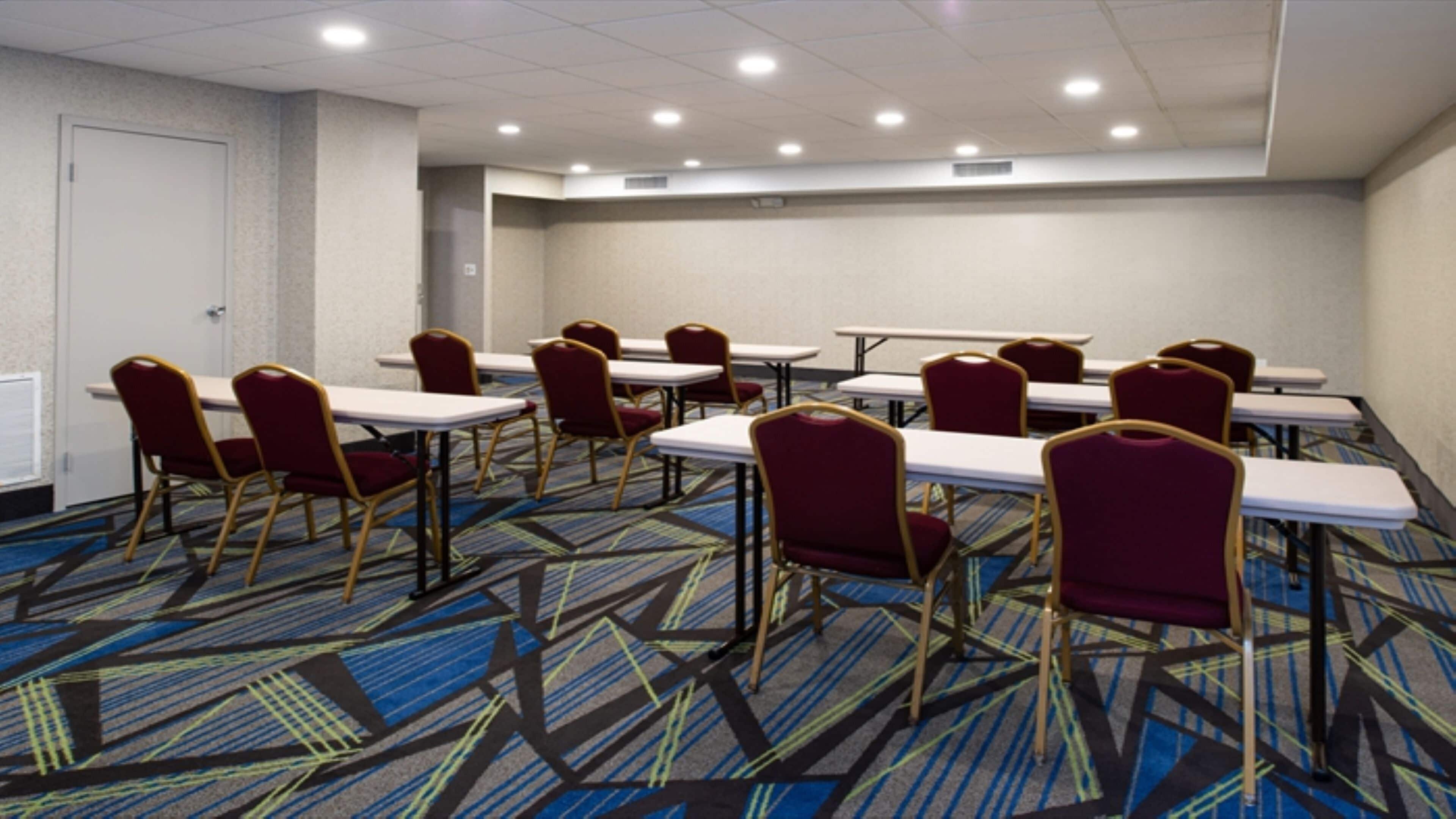 A conference room with tables and chairs, carpeted floor, and ceiling lights.
