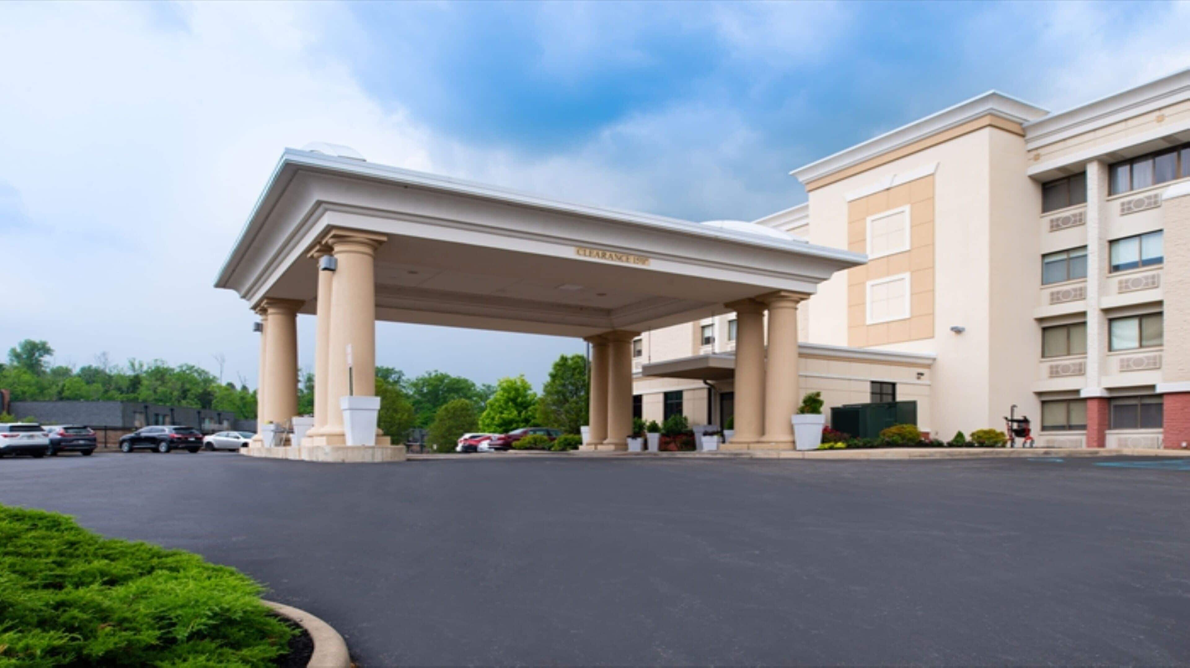A hotel with a covered entrance, multiple floors, and a parking lot.