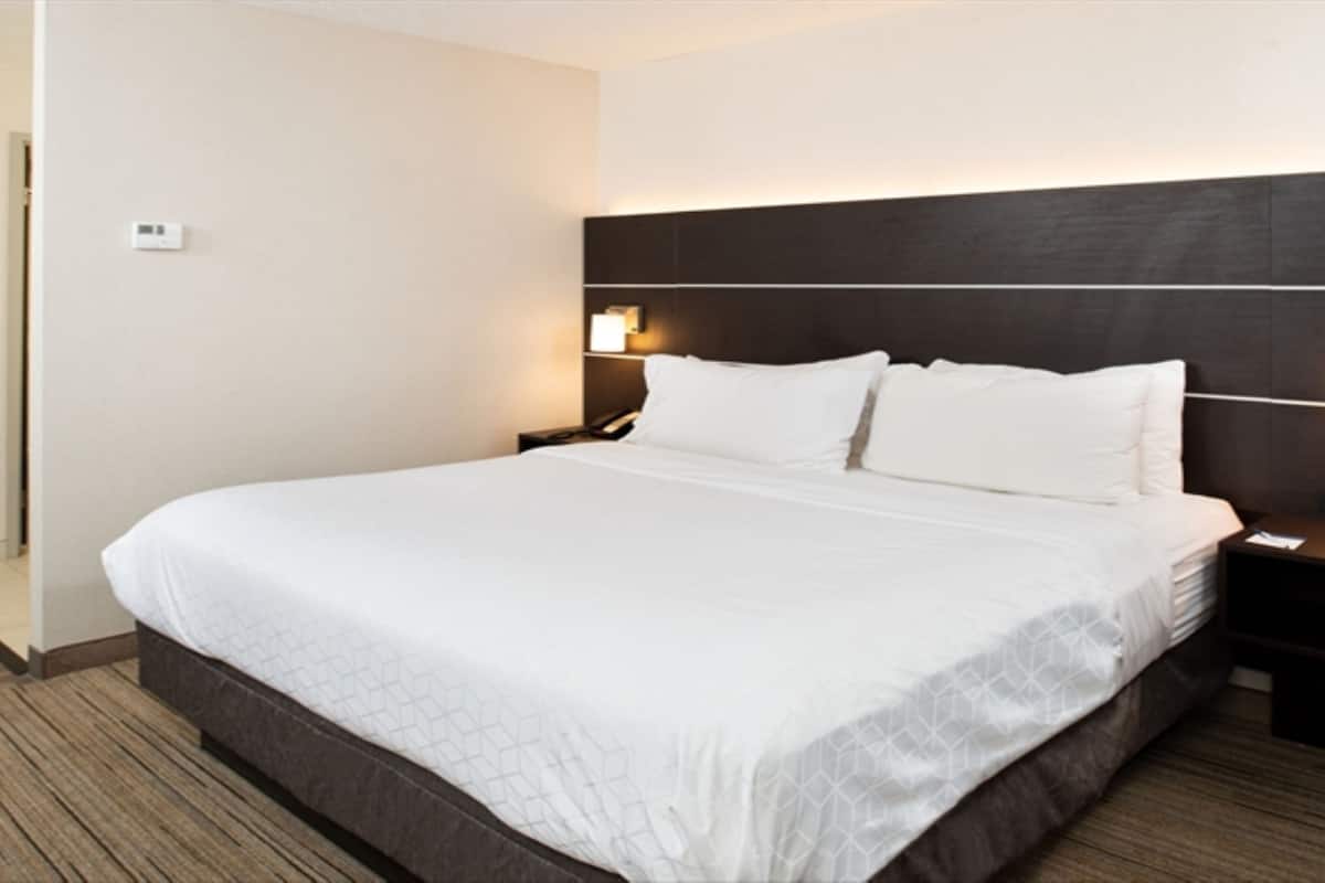 A hotel room with a large bed, two bedside tables, and a wall-mounted light fixture.