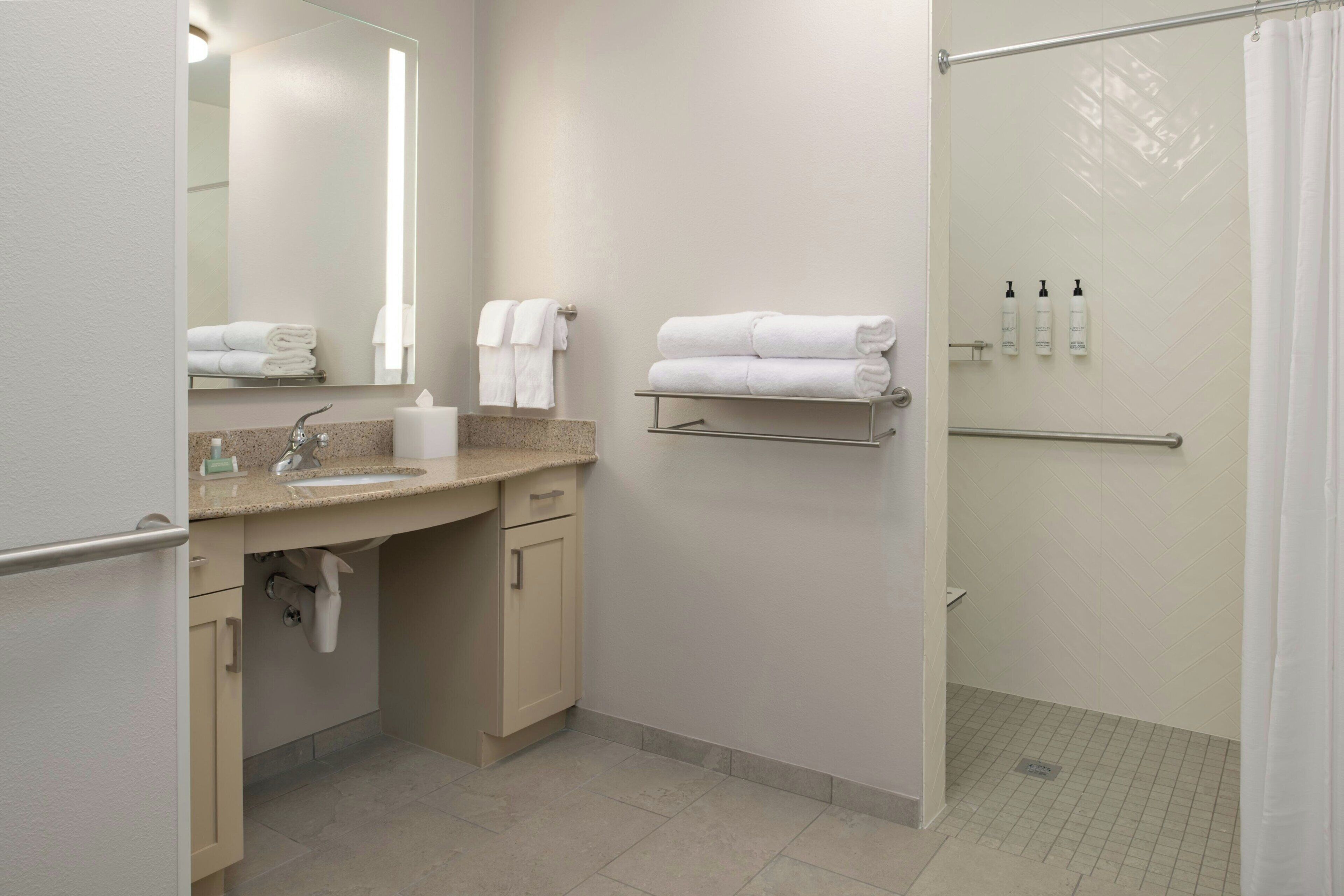 Baño con lavamanos, espejo, toallero y zona de ducha.