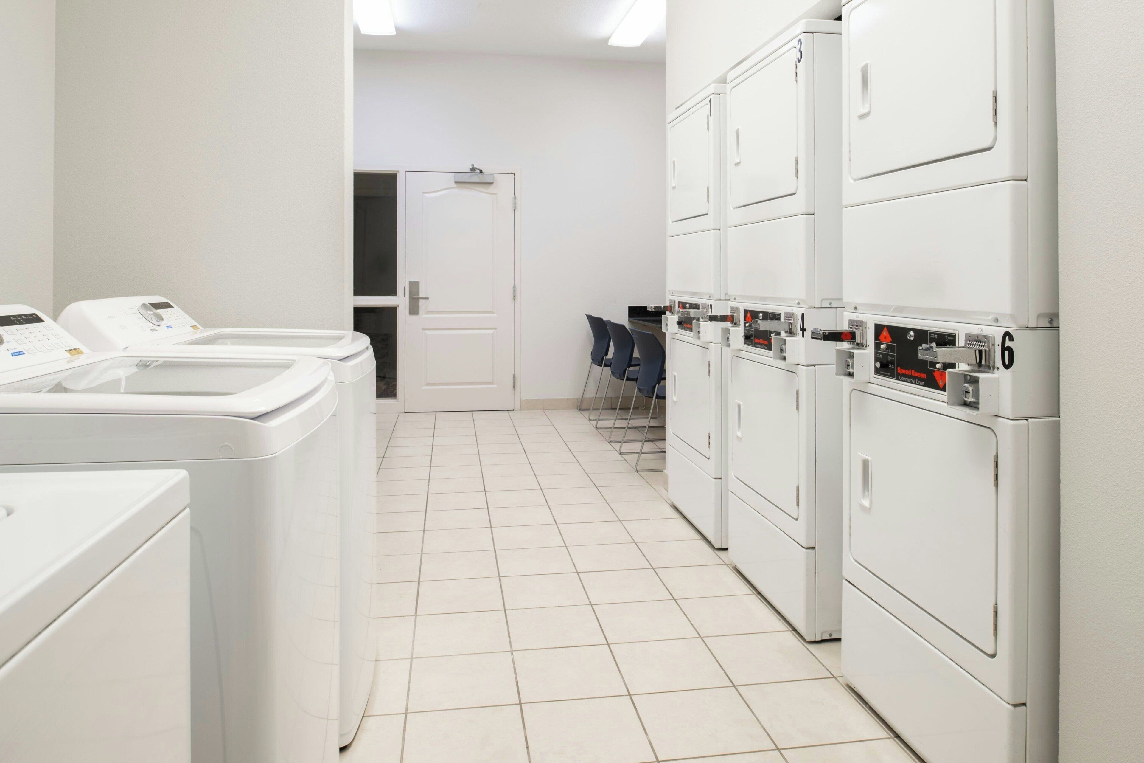 A laundry room with multiple washing machines, a door, and chairs.