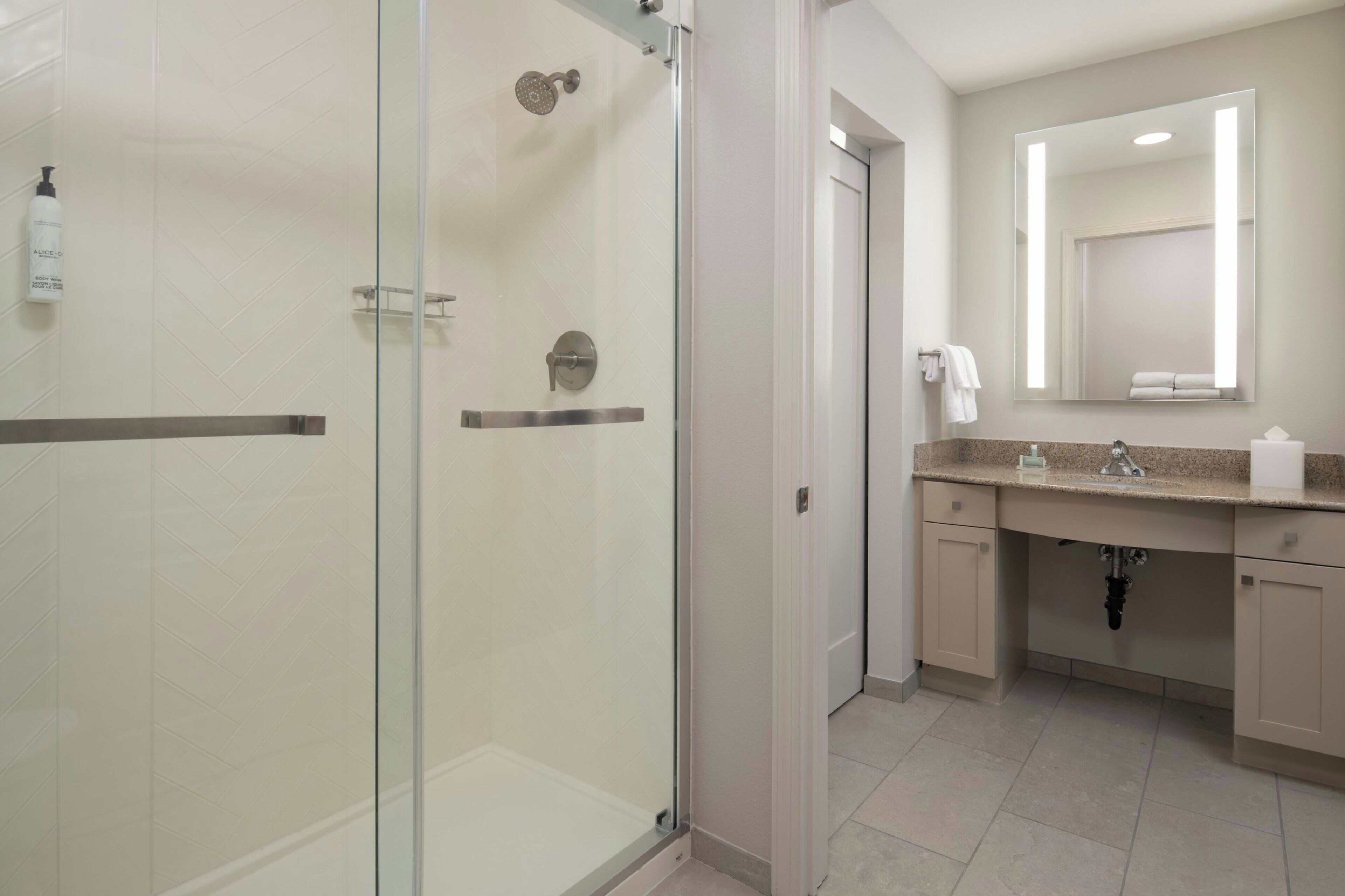 Un baño moderno con ducha envuelta en cristal, un lavabo con espejo y un perchero para toallas.