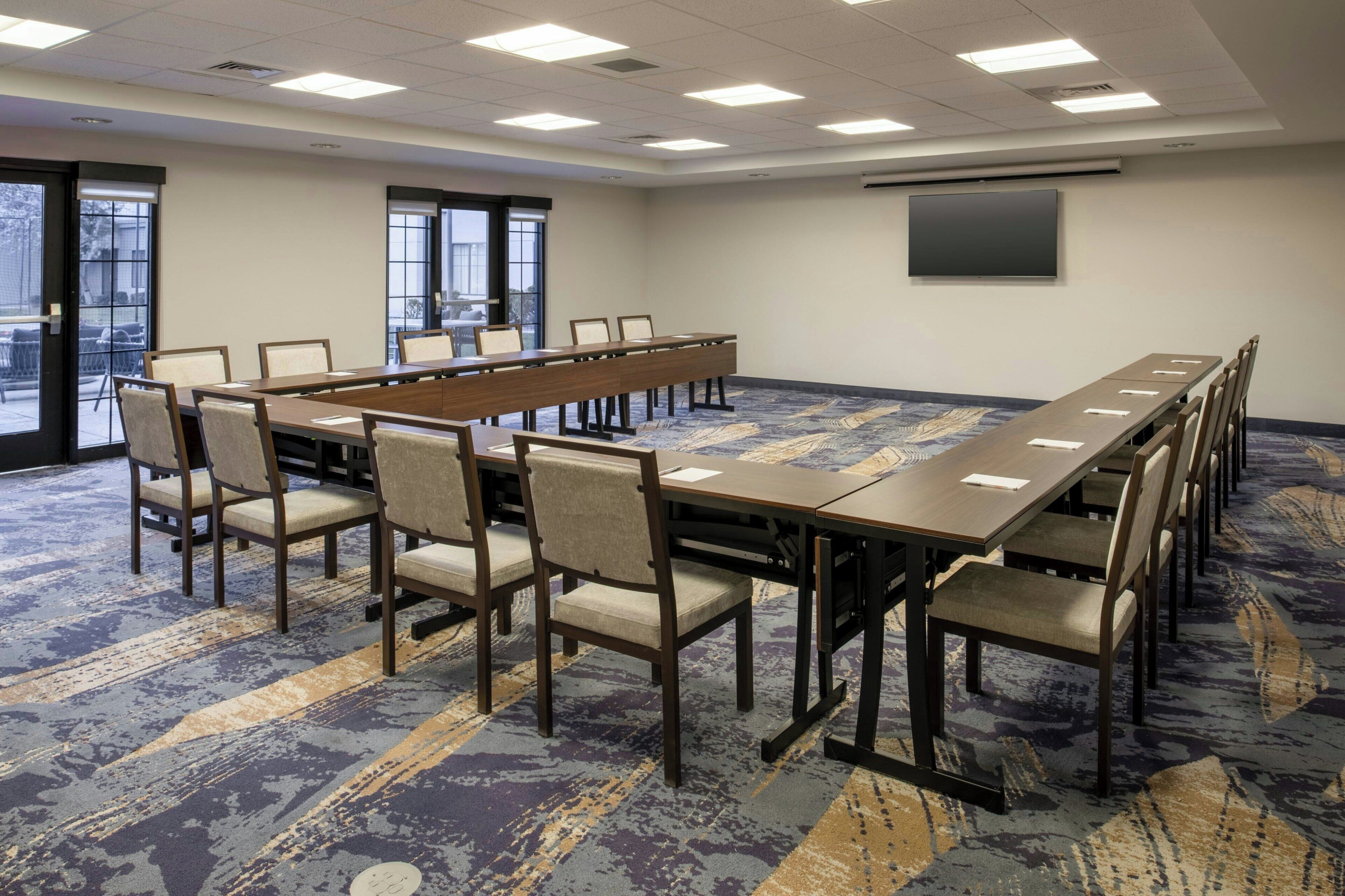 A conference room with a long table, chairs, a projector screen, and large windows.