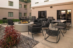 Eine Terrasse mit Sitzgelegenheiten im Freien, einer Feuerstelle und einem Gebäude mit mehreren Fenstern.