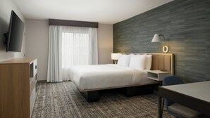 A hotel room with a bed, a desk, a chair, a TV, a lamp, and a window with curtains. - TownePlace Suites by Marriott Reno (Reno)
