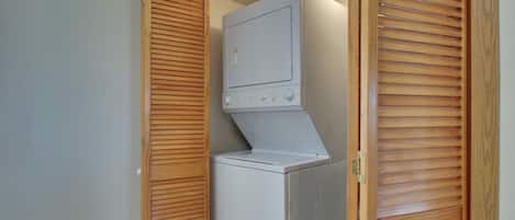 A compact laundry room with a built-in washer and dryer, wooden louvered doors, and a visible electrical outlet.